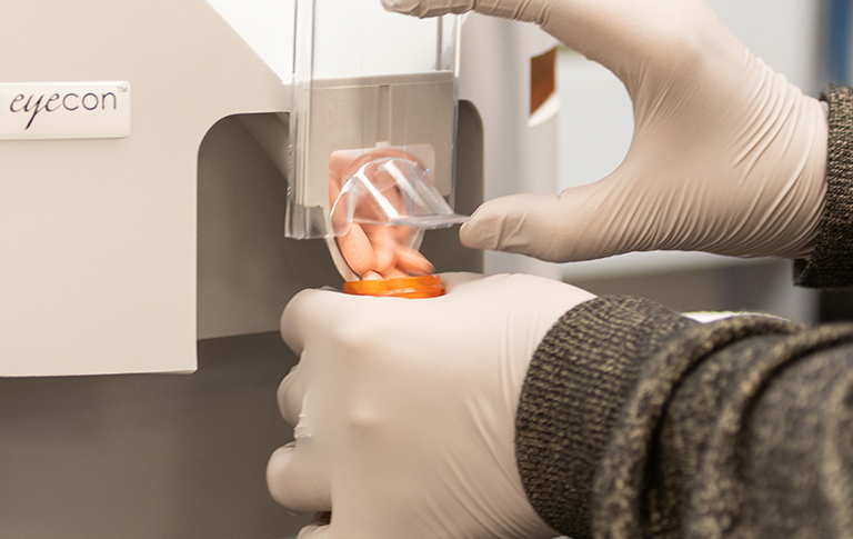 Pharmacist in white gloves pouring tablets into pill bottle using machine.