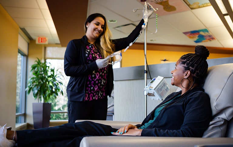 Nurse holding IV pole while smiling with smiling patient.