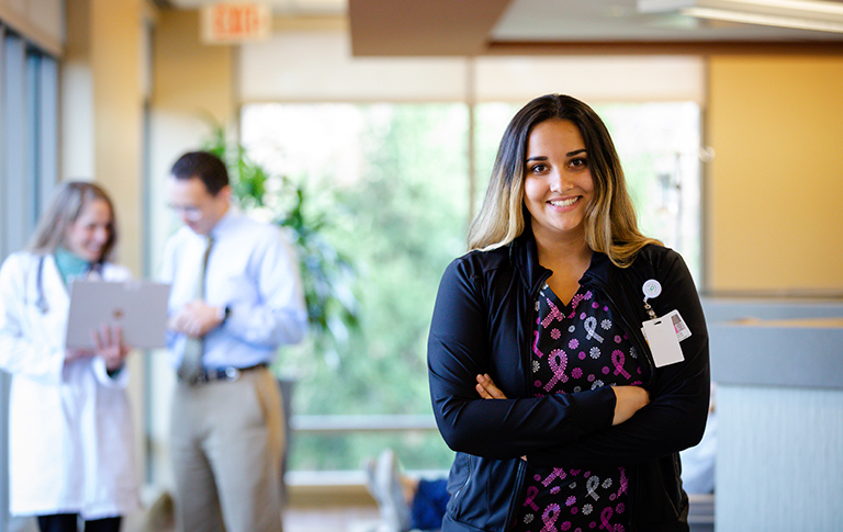 Smiling nurse with arms crossed. Doctors in background.